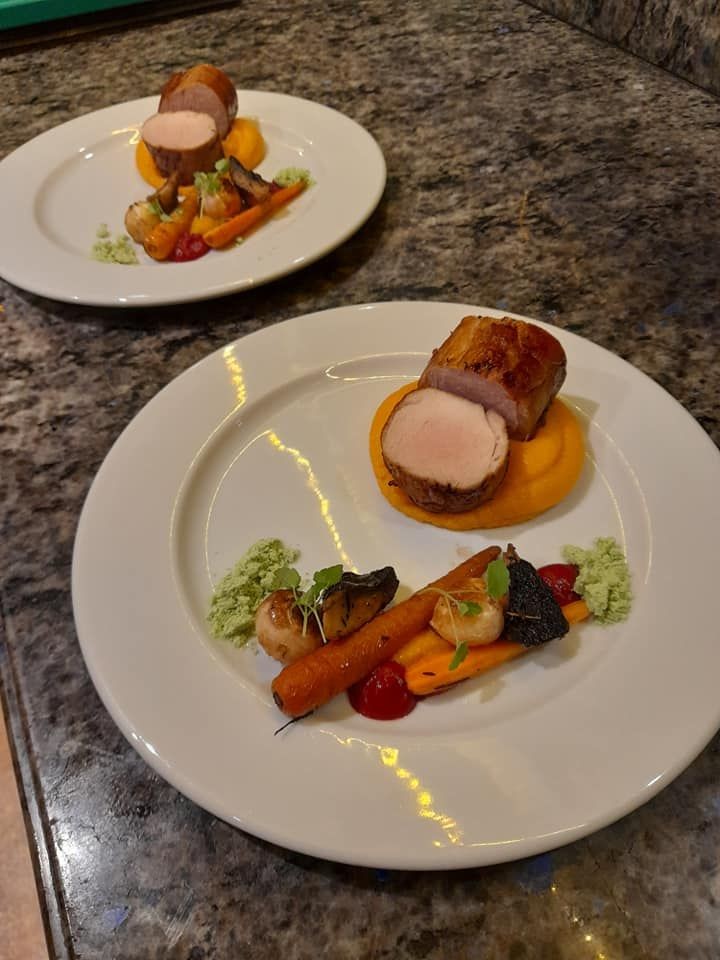 Two plates of gourmet pork tenderloin with carrot puree and vegetables on a stone countertop.