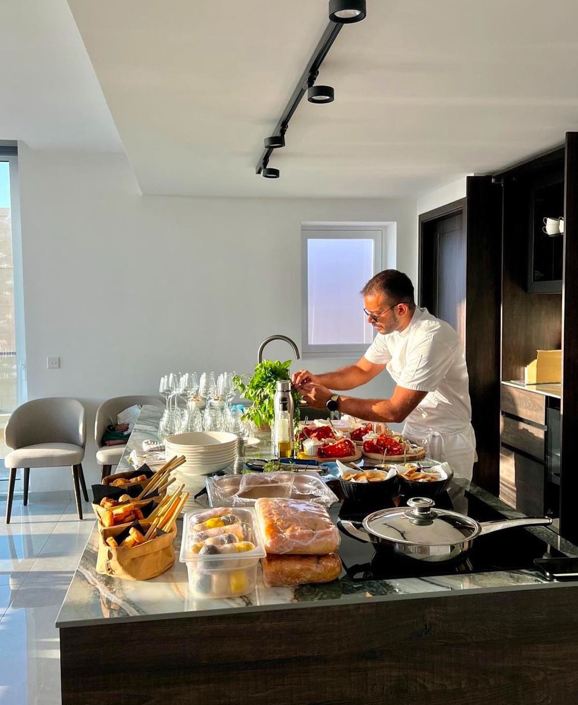 Chef preparing food at a kitchen counter with various dishes and ingredients in a modern kitchen.